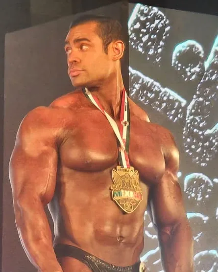 Bodybuilder on stage wearing a medal with the colours of Mexico